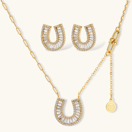 Gold-plated horseshoe necklace and earring set with baguette and round crystals arranged in geometric pattern on white background.